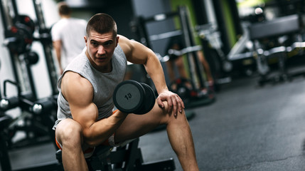 Fototapeta na wymiar Fit man in sportswear focused on exercise for biceps in the gym