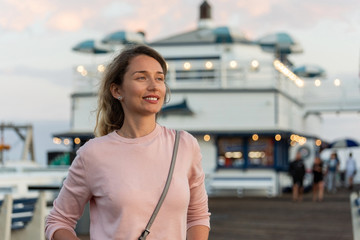 Happy blonde woman in pink sweater at the pier of Malibu