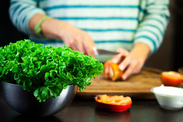 Girl cuts the tomato on the wooden cutting board