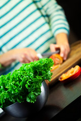 Girl cuts the tomato on the wooden cutting board