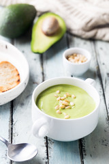 bowl of broccoli and green peas cream soup in a white bowl with avocado