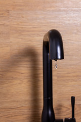 Small water drop from kitchen modern black tap. Vertical photo. Saving water concept. Selective focus. Dripping kitchen faucet. Unnecessary waste of water in the world.