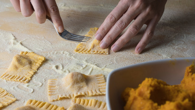 Closeup process making ravioli vegan homemade pasta. Housewife cook closes with a fork 'tortelli di zucca', traditional italian pasta, woman cooking food on kitchen