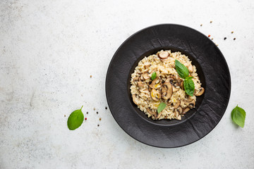 Risotto with mushrooms in a black plate over white background, top view