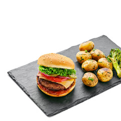 Hamburger with grilled vegetables and scallion served on a stone black board isolated on white background.
