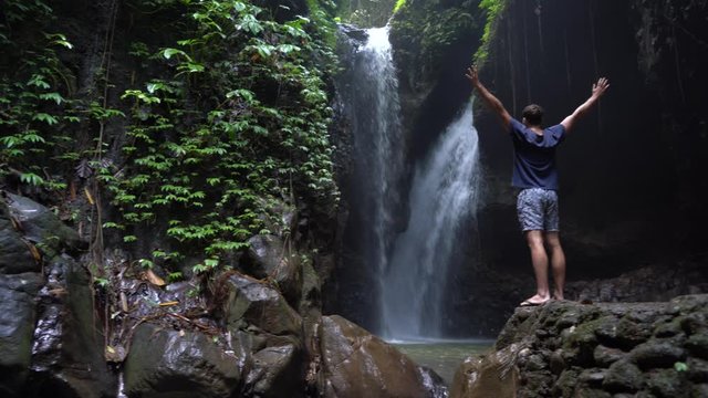 Adventurous man and enjoying the beautiful view during a vibrant sunrise. Detail of the Gitgit waterfall at Bali, Indonesia