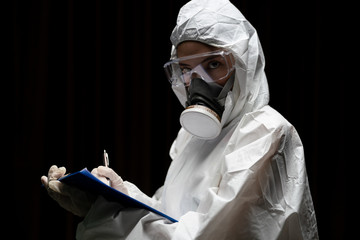 Woman wearing gloves with biohazard chemical protective suit and mask. is writing report on paper.