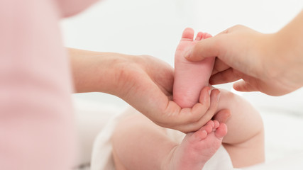 Baby massage. Female therapist gently massaging babys foot. Mother touching her newborns bare feet, bonding time. Reflexology concept.