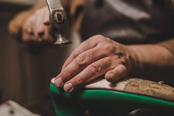cropped view of shoemaker holding hummer while repairing shoe in workshop