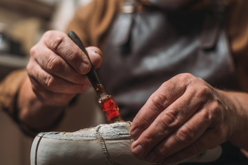 cropped view of shoemaker applying glue on shoe with brush - Powered by Adobe