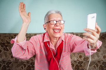 Happy old lady having a skype call on her cellular - obrazy, fototapety, plakaty