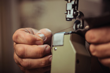 cropped view of cobbler holding thread while sewing leather on sewing machine