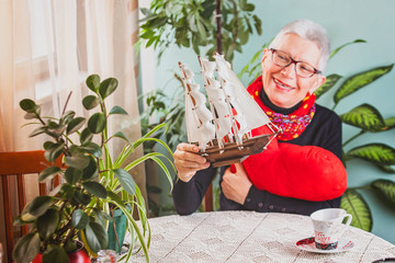 Cheerful old lady playing with small galleon ship and heart shaped pillow