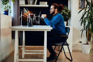 Side view of attractive bearded entrepreneur sitting in his office, relaxing and drinking coffee.