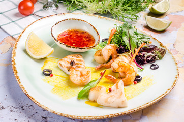 Closeup of grilled shrimp with red chili pepper sauce, vegetables at a table background.