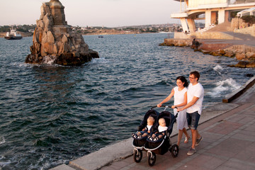 Happy family walking with twins buggy on promenade against the sea.