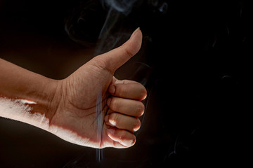A close up of a man's hand showing a thumbs up and smoky black background