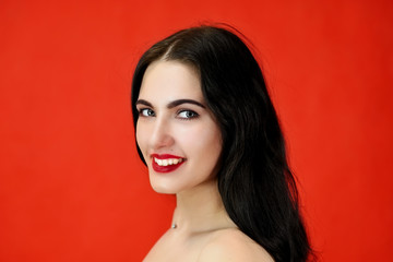 The concept of excellent makeup and cosmetics. Close-up Portrait of a pretty brunette model girl with excellent makeup and luxurious hair on a red background in the studio.