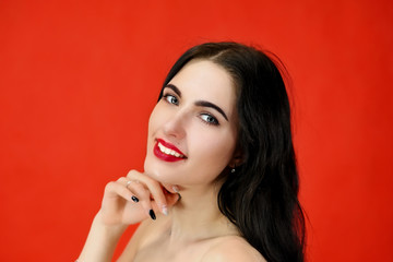 The concept of excellent makeup and cosmetics. Close-up Portrait of a pretty brunette model girl with excellent makeup and luxurious hair on a red background in the studio.