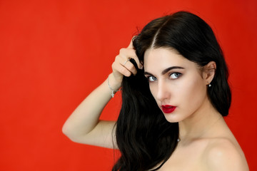 The concept of long beautiful hair. Close-up Portrait of a pretty brunette model girl with excellent makeup and luxurious hair on a red background in the studio.