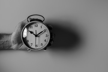 A business man holding a white alarm clock on a white background.