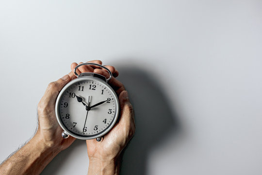A business man holding a white alarm clock on a white background.