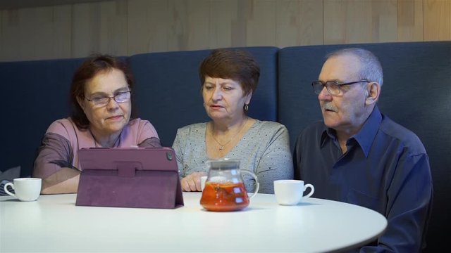 Senior Friends Viewing Photo Album on Tablet Computer while Sitting in Cafe. Technology, Retirement Age, Memories and People Concept