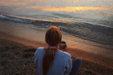 Naklejka na ściany i meble Girl with a cup of coffee by the sea at sunset