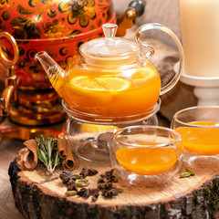Sea Buckthorn tea candle basking in Russian restaurant. Vitaminic healthy sea buckthorn tea with cinnamon, lemon, rosemary, honey on wooden background.