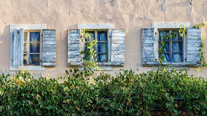 Fototapeta na wymiar Old vintage windows with closed curtains and open white-blue shutters on the textured wall of very old house.