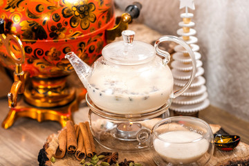 Traditional Indian tea in the teapot candle basking with milk and aromatic spices masala chai and cup on wooden background. Food and drink. New year holidays, christmas xmas concept