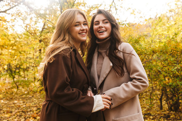 Two cheerful young pretty girls wearing coats walking together