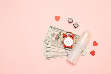 Fototapeta na wymiar A lot of dollars, clock alarm, cube heart shape decor and lubricant on a pink background. Love for money concept
