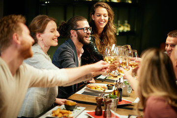 Best friends sitting in restaurant for dinner and making a toast with white wine. On table is food.