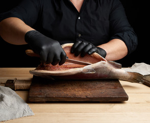 chef in black uniform and black latex gloves cuts a carcass of fresh salmon fish