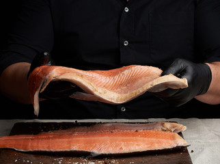 Obraz premium chef in a black shirt and black latex gloves holds a large piece of salmon fish fillet
