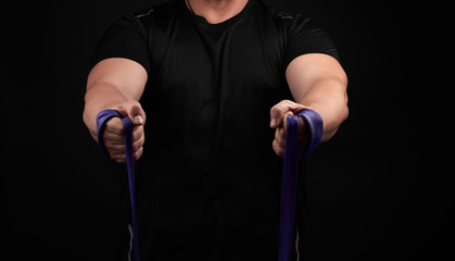 athlete with a muscular body in black clothes is doing physical exercises with purple rubber