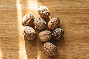  Solid and embossed brown-shelled walnuts lie on a wooden table, illuminated by the harsh sunlight