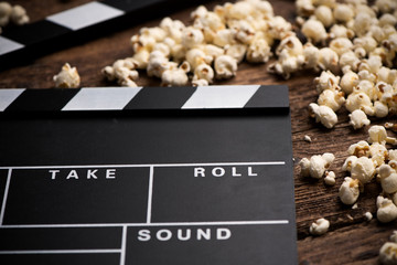 Clapper board and popcorn on wooden background