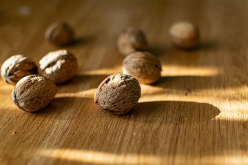  Solid and embossed brown-shelled walnuts lie on a wooden table, illuminated by the harsh sunlight