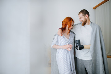 Happy husband and wife standing together, drinking coffee at home. Smiling. Man has a prosthetic...