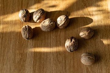  Solid and embossed brown-shelled walnuts lie on a wooden table, illuminated by the harsh sunlight