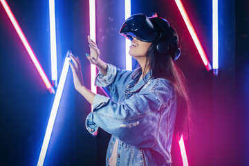 Mod curly dark haired girl dressed in blue denim jacket uses the virtual reality glasses on her...