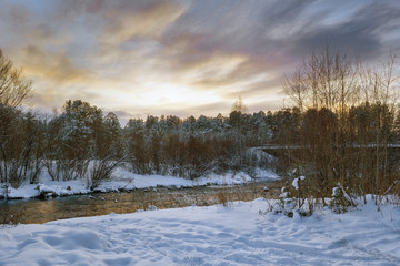 Winter landscape at sunset by a snowy forest lake. Winter forest.