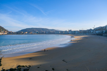 The huge sandy beach in the bay of San Sebastian, is considered the best in the world. People walk along the beach in the early morning on a clear sunny day in winter on the Atlantic coast of Spain.