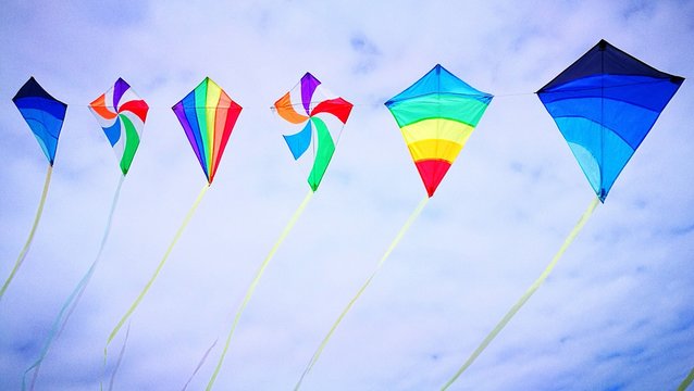 Low Angle View Of Colorful Kites Flying Against Cloudy Sky