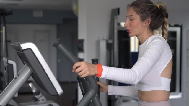 Woman in white sport suite running on fitness machine at the club