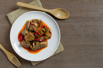top view of stir fried duck meat with red curry paste in a ceramic dish on wooden table. hot and spicy thai style food menu.
