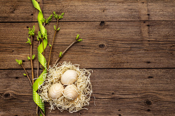 Zero waste Easter concept. Spring twigs with fresh green leaves, wooden eggs in nest, polka dot ribbon. Old vintage wooden boards background