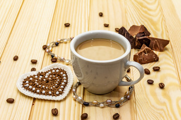 Valentine's Day concept. Cup of coffee, chocolate, knitted heart, string of pearl beads. Romantic breakfast and gift on wooden boards background, copy space